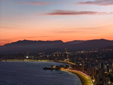 Manzaralı sahil manzarası, sakin körfezin üzerindeki akşam ışıkları, insansız hava aracı huzurlu sahil kıyılarını yakalıyor.