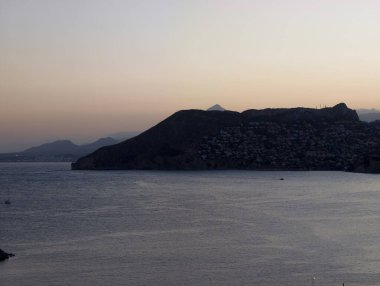 Dağ arkaplanlı sessiz bir koy, sakin bir gece, yansıtıcı sularla ve seyreklikle burunda