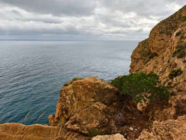 Uzak kayalık kayalıklar, karanlık bulutların altındaki fırtınalı suların yalnızlığını ve manzarasını sunuyor.