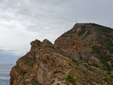 Fırtınalı denizlere bakan kayalık kayalıklar çalkantılı gökyüzüne karşı yükseliyor ve köpüklü dalgalar çarpıyor.