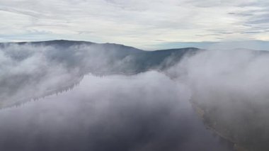 Suyun örtülü gövdesine sahip esrarengiz bir manzara, karanlık kıyı şeritleri ve nazik ağaç hatlarıyla rüya gibi bir manzara.