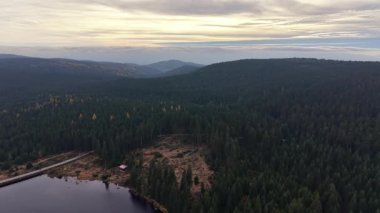 Yüksek görüş açısı, katmanlı tepeler ve rezervuar üzerindeki gün batımı, uzak suyu ve akan araziyi gösteren sakin manzara