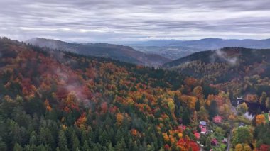 Mevsimlik renklerin yer aldığı geniş tepe manzarası bulutlu gökyüzünün altındaki renkli tepelerin arasına kurulmuş uzak köy.