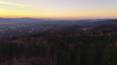 Orman bekçisi alacakaranlıkta ufuk gözlüyor, sakin akşam manzarası yuvarlanan tepeler ve parıldayan köy ışıkları