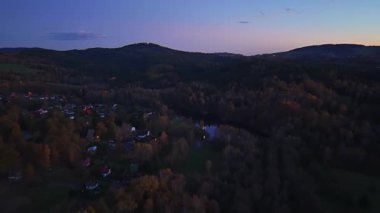 Akşam ışıkları tepenin üzerinde, alacakaranlık aydınlık köyler ve dolambaçlı kır yolları ile yerleşir.