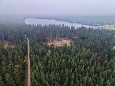 Su deposu ve ormanın drone görüntüsü, ağaçların arasından geçen dar yol sisli arka plan ve katmanlı tepeler,