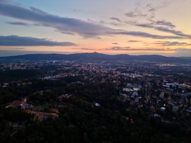 Yeşil Tepelerin Üzerindeki Günbatımı Şehir, Parlayan Çatılar Ve Uzak Işıklı Sıcak Bulutlar, Sakin Atmosfer
