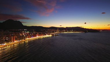 Alacakaranlıkta kıyı silueti aydınlandı, İHA 'lar canlı bulvarları tarıyor ve parlayan deniz, yansıyan şehir ışıkları...