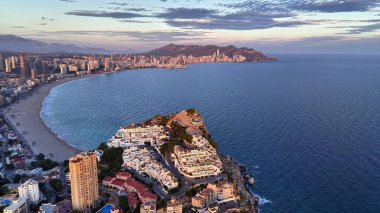 Alacakaranlık turuncu ışıkta beyaz kayalıkların tepesindeki evlere bakan kıvrımlı körfeze bakan uçurum kenarındaki tepe.