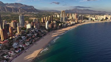 Canlı sahil kenti üzerinde gün ortası havası. Yükseliş yoğunluğu altın kum, turkuaz okyanus, hareketlilik.