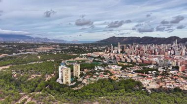 Körfez ve sahil manzaralı kıyı şeridi, şehir genişlemesi ormanlık tepenin arkasında görülebiliyor, planlayıcı denetliyor.