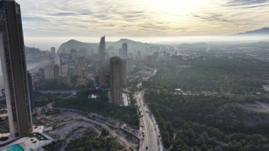 Şafak vakti şehre yaklaşır, dolambaçlı arter yolu dramatik gökyüzü altında uzak kulelere çıkar, sinematik