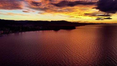 Sessiz koyda turuncu gün batımı, kıyı araştırması için kullanılan hava görüntüleri, kehribar gökyüzünü yansıtan hafif dalgalar.,