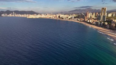 Şafak vakti silip süpüren okyanus eğrisinin üzerindeki hava sükuneti cam su, ince dalgalar, uzak şehir silueti