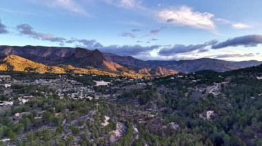 Kasabalı altın dağ vadisi, güneşli tepeler çam ormanları üzerine sıcak ışık saçıyor, dolambaçlı yollar.