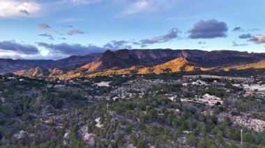 Güneşli dağ kasabasının havadan görünüşü, tepelerdeki altın ışık, çam eteklerindeki dağınık evler, dramatik.