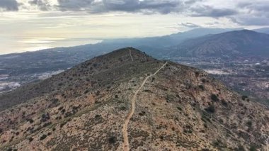 Vadi ve denize tepeden bakan güneşli tepe. Kayalık yamaçlarda ve dolambaçlı yollarda altın saat parıldıyor.