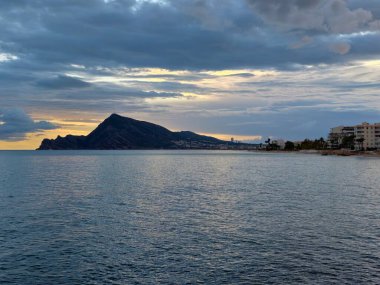 dramatik bulut katmanları sivri burnun üzerinde yuvarlanıyor ve sakin deniz, gün batımı bulutları kırıyor.
