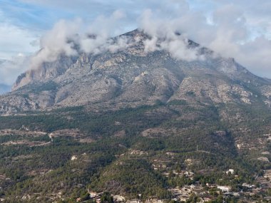 Orman yamaçlarının ve dağınık konutların üzerinde beliren bulutlu zirve dramatik gökyüzü ve dokulu kaya yüzeyleri