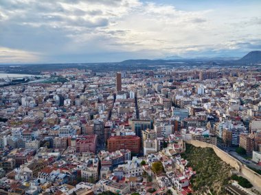 Alacakaranlık kıyısı şehri sıcak akşam parlaklığı, uzun gölgeler, yoğun bloklar, uzak deniz ipuçları ve dramatik