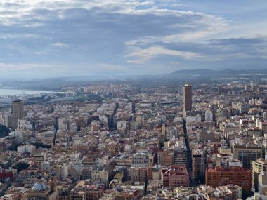 Uçurum kenarındaki tepede kentsel yayılma ve uzak dağlar, engebeli kaya önplanı, güneş ışığı blokları ve derin