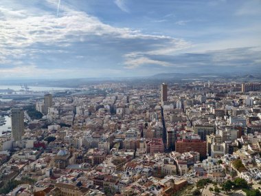 Limanı ve yoğun çatıları olan havadan şehir manzarası, marina ve liman kuleleri, bulutlu gökyüzü yumuşak ışığı yansıtıyor,