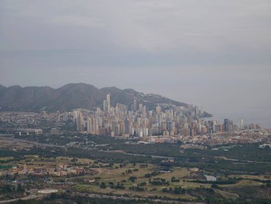 Uzak kıyı şeridi olan dağlar tarafından çerçevelenmiş metropol, yoğun kule kümesi, yuvarlanan alanlar ve kırsal