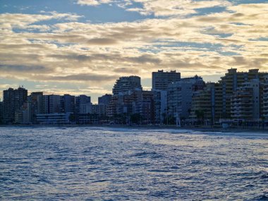 Altından gündoğumu kıyısı dalgalı ufuk çizgisi, günışığı yükselen binalar kıyı şeridi boyunca uzanan, parıldayan