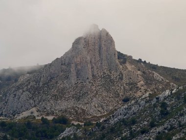 Puslu kireçtaşı zirvesi engebeli araziye hükmediyor. Uçurumları saran alçak bulutlar ve dağınık çam ağaçları serin.