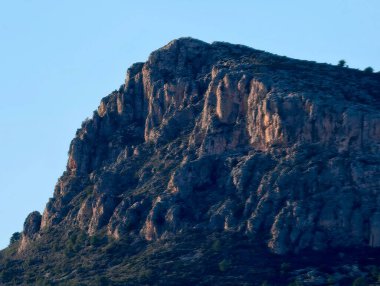 Güneşli kayalık zirve, mavi gökyüzüne karşı yükseliyor kayalıklarda ve tepelerde sıcak röfleler, izole taş yığınları
