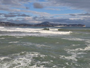 Uçsuz bucaksız deniz manzarası dalgalanan dalgalar ve ufuktaki uzak tepeler katmanlı bulutların altında geniş açık sular.