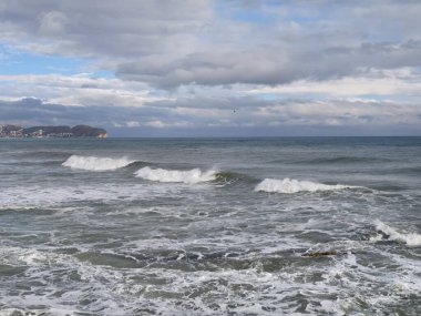 Kıyı manzarası dalgalı ve ufukta uzak şehir, şehir silueti katmanlı deniz manzarası