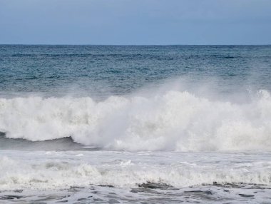 Kükreyen okyanus dalgaları kıyıya çarpıyor, fırtınalı gri gökyüzü ve çalkantılı köpük dramatik atmosfer yaratıyor, ideal