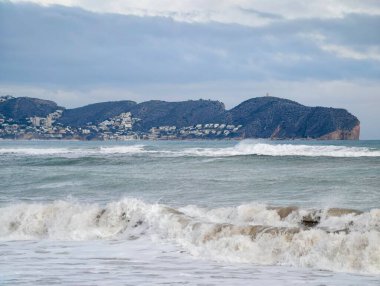 Lowangle deniz manzarası köpüklü sörf ve ufukta uzak bir pelerin, açık su ve kayan bulutlar yaratır.