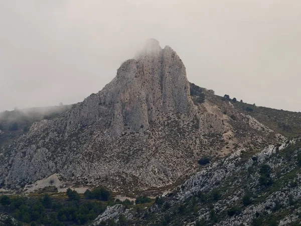 Puslu kireçtaşı zirvesi engebeli araziye hükmediyor. Uçurumları saran alçak bulutlar ve dağınık çam ağaçları serin.