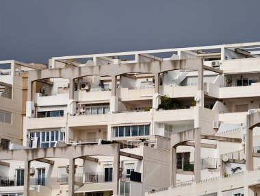 Gölgeli güneşli apartman terasları, eskimiş beton korkuluklar, çizgili tenteler, saksılı otlar ve arka bahçeler.