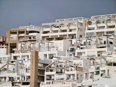 Bulutlu gökyüzünün altında istiflenmiş apartman balkonları, tek renkli bej cepheler tekrarlayan geometrik ritim yaratıyor