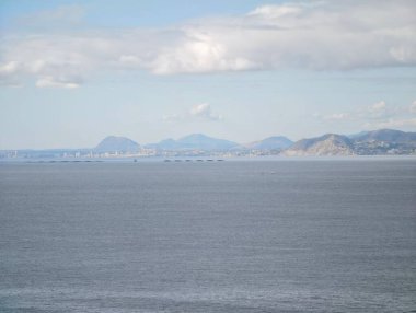 Uzak dağlar sakin denizin üzerinde süzülür, yumuşak bulutlar ve sessiz ışık meditasyon yapan kıyı manzarası yaratır, mükemmel.