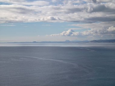 Yumuşak bulutların altında ışıldayan sakin su, hafif parıltı ve pastel tonlarda geniş denizde rahatlatıcı kompozisyon.