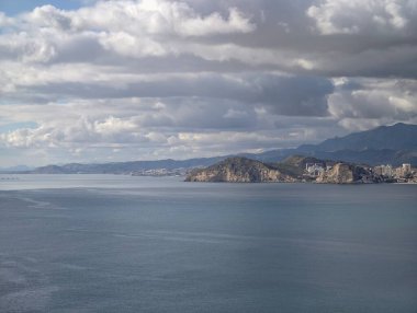 Kayalık kayalıklar körfeze iniyor, yığılmış binalar ve dağ arka planı, sakin kıyı şeridi