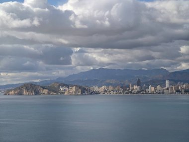 Sakin kıyı koyunun üzerinde kara kara düşünen gökyüzü, durgun turkuaz su üzerinde ağır bulut oluşumları, uzak kuleler