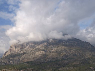 Bulutlu dağ zirvesi dalgalı bulutlar ve engebeli kireçtaşı yamaçlar, yeşil manzaralı hava manzarası