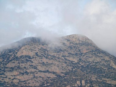 Gri gökyüzünün altında gizlenmiş granit tepeler, aşınmış kaya yüzleri ve sarmaş dolaş bulut dalları.,