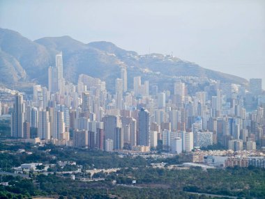 Sisli dağ yamaçları ile çevrelenmiş yoğun şehir kuleleri sessiz ışık ve katmanlı kentsel formlar, atmosferik