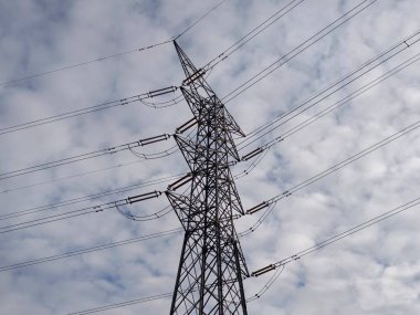 Kumaşlı bulutlar üzerinde güç pilonu geometrisi, güçlü dikey çizgiler ve tekrarlayan kablolar soyut desen oluşturur,