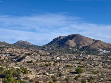 Uzak tepelere doğru uzanan kuru çalılıklar, seyrek bitki örtüsü, kayalık topraklar ve geniş mavi gökyüzü kuraklığı çağrıştırıyor