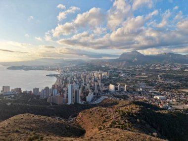 Sahil kenti üzerinde gün doğumu sakin okyanusa, kümelenmiş kulelere yansıyan altın ışıkla birlikte ufuk çizgisi üzerinde.