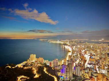 Hava kıyı şeridi alacakaranlıkta ufuk çizgisinde aydınlık sahil kuleleri ve kavisli gezinti güvertesi, sıcak alacakaranlık