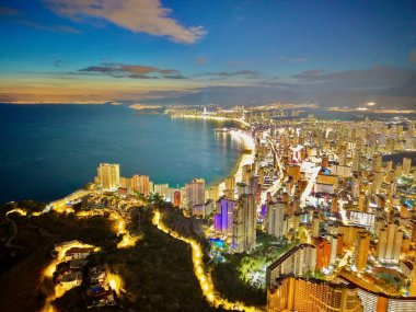 Neon ışıklarıyla aydınlatılan kıyı silueti yüksek pencereli, çatısı teraslı çalışma ortamı sunuyor.