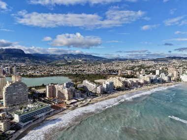 Süpürücü şehir manzarası ve uzak dağları, sahil kuleleri ve kıvrımlı körfezi olan havadan turkuaz körfez.